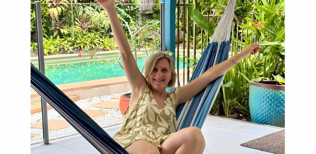 Australian artist Frauke Claire in a hammock, arms raised with joy, pool and tropical plants behind her
