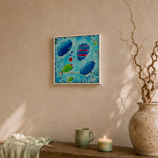 Modern abstract painting in blue with round shapes on a sunlit wall above a bench with a cup, candle and face with branches. 