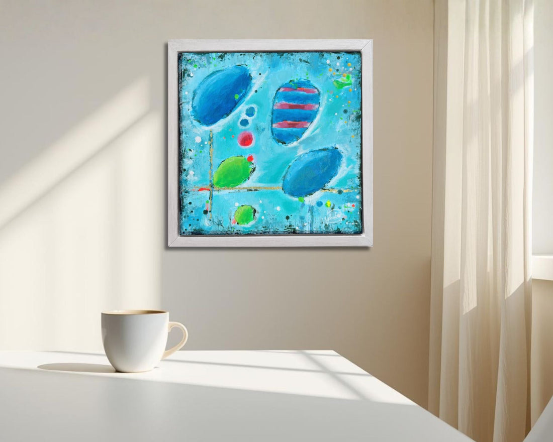 Modern abstract painting in blue with round shapes on a wall above a table with a cup on it.