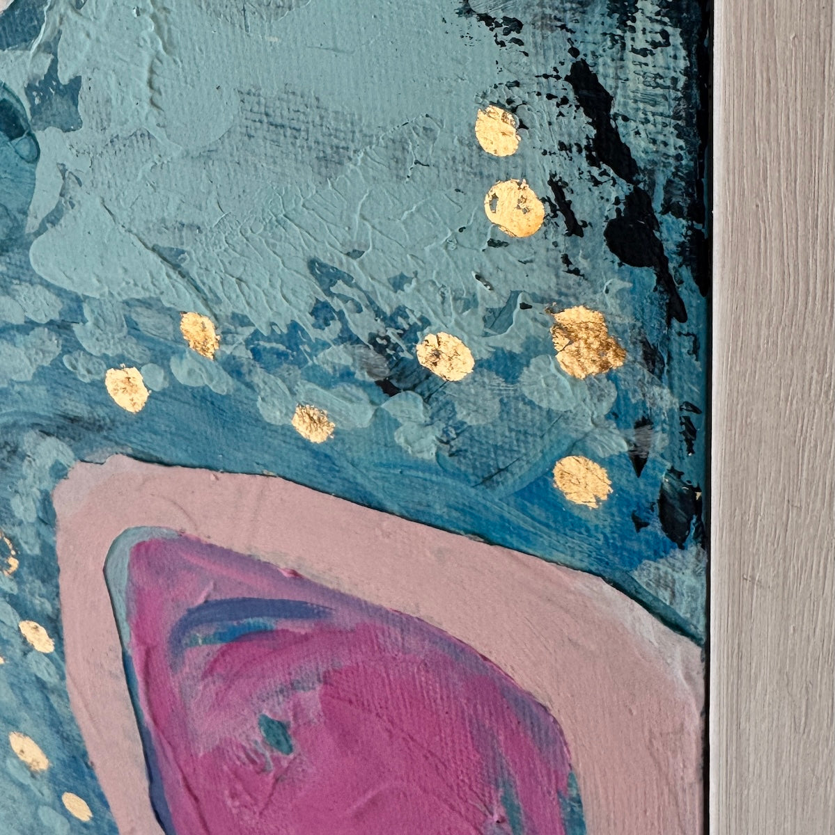 Abstract painting detail with textured blue and teal areas, gold metallic art dots, a pink and purple curved shape, and a light wood panel along the right edge.