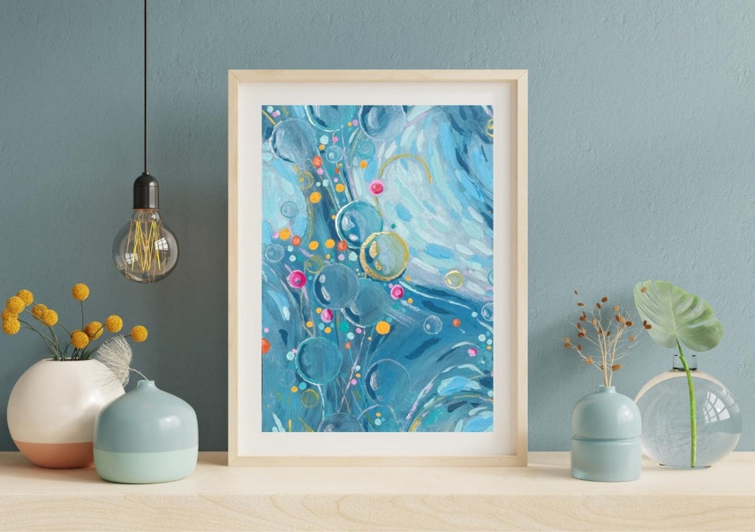 Framed abstract artwork with blue swirls and colorful dots on a wall with decorative items.