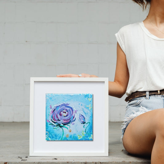 Person holding a framed painting of a blue rose with a white background