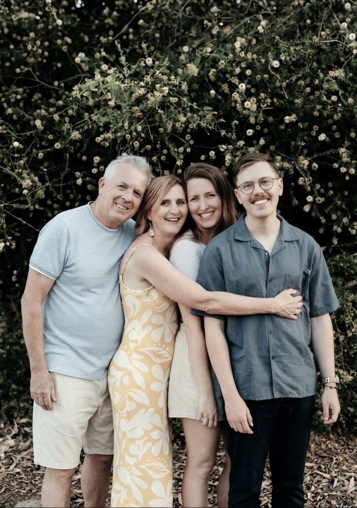 Family of four posing outdoors with greenery in the background