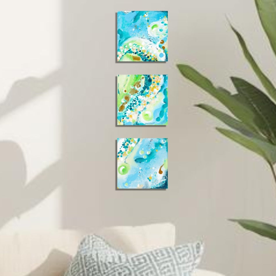 Three square wall art set with abstract blue and green designs on a sunlit wall.