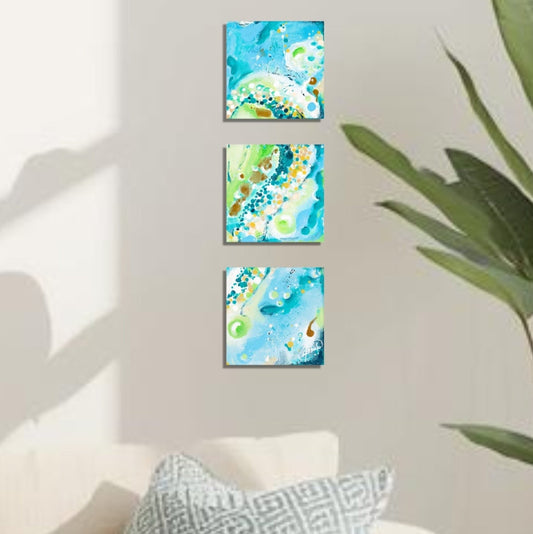 Three square wall art set with abstract blue and green designs on a sunlit wall.
