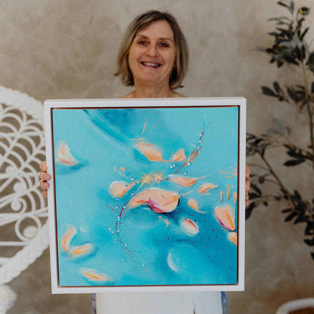 Woman holding A Glowing Change - blue turquoise abstract square canvas with white floating frame and soft peach shapes by Frauke Claire