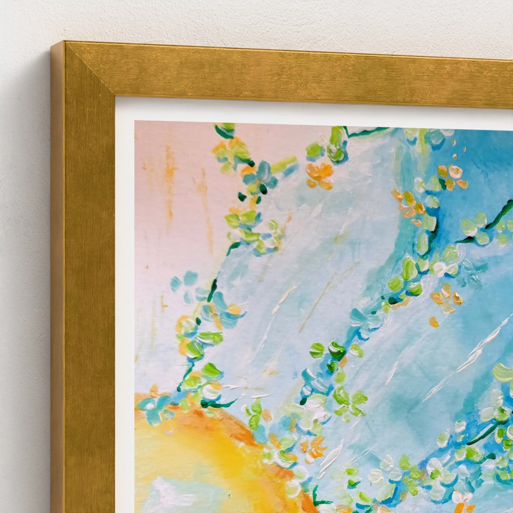 A close-up of a gold framed abstract floral art print with blue, green, yellow, and white brushstrokes, set in a textured gold frame against a white wall.