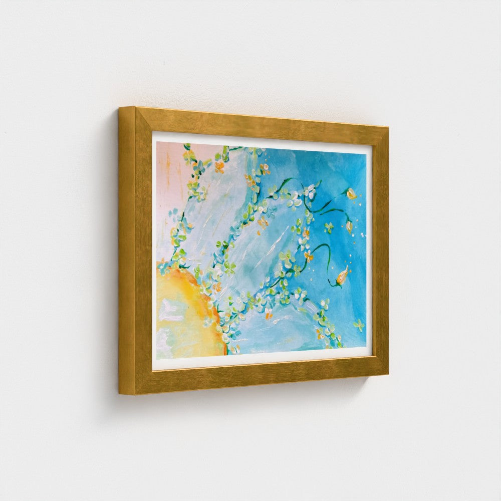 Framed abstract floral art print with blue sky-like background, white blossoms, yellow accents, and a gold frame hanging on a light gray wall.