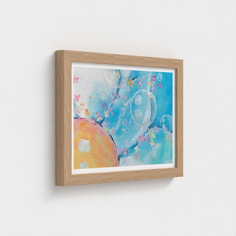 Framed abstract wall art hanging on a light gray wall. The artwork features a bright blue background with bubble-like circular forms, soft pink floral details, and a peach-orange oval shape.