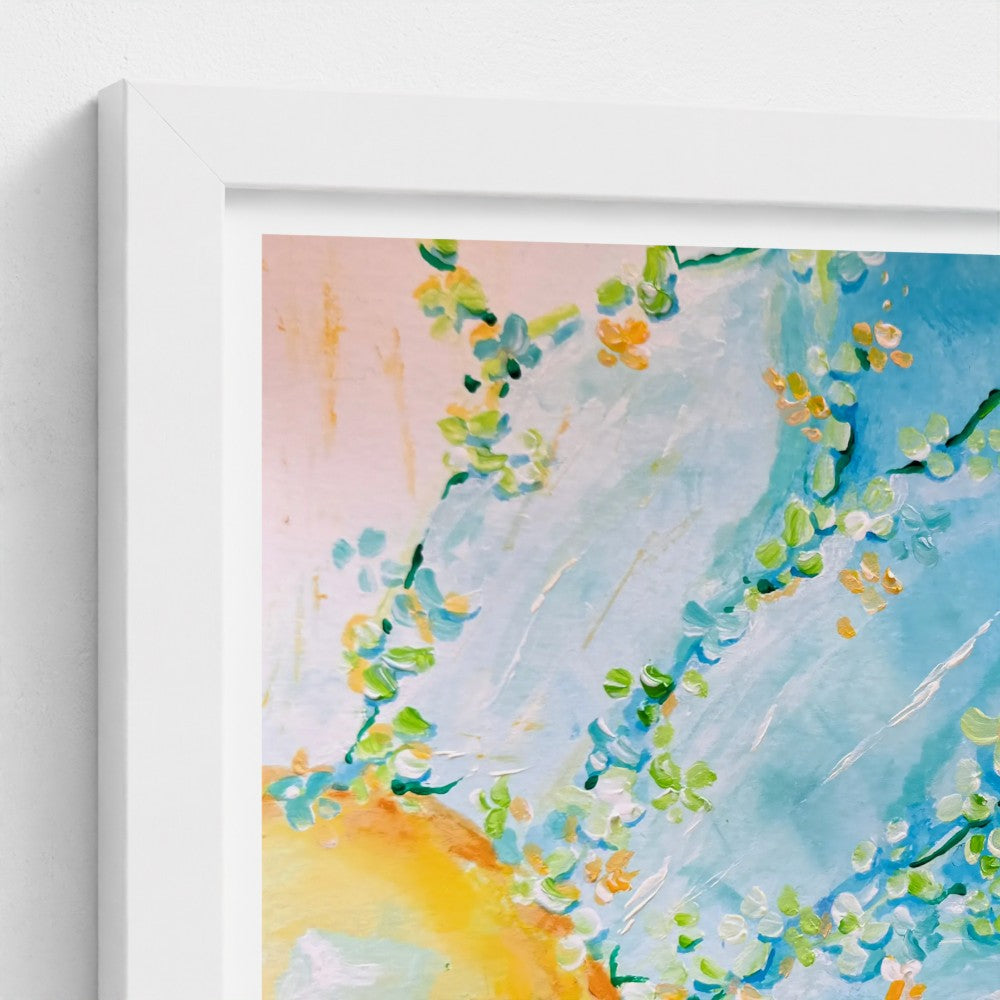 A close-up of a white framed art print featuring a watercolor-style floral design with blue, green, yellow, and soft pink tones, shown against a white wall.